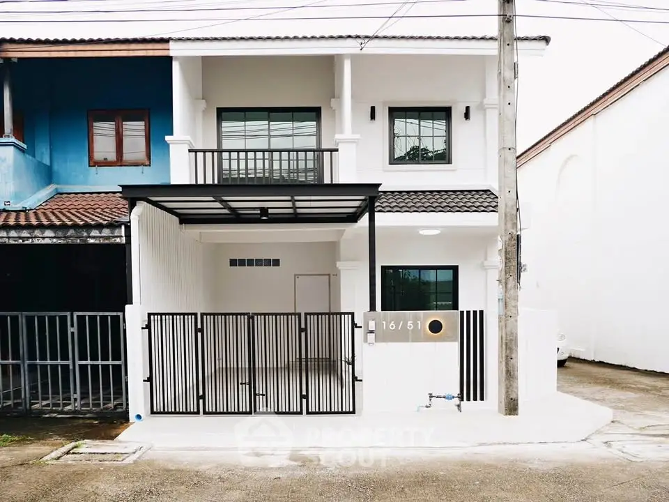 Modern two-story white house with gated entrance and balcony in a suburban neighborhood.