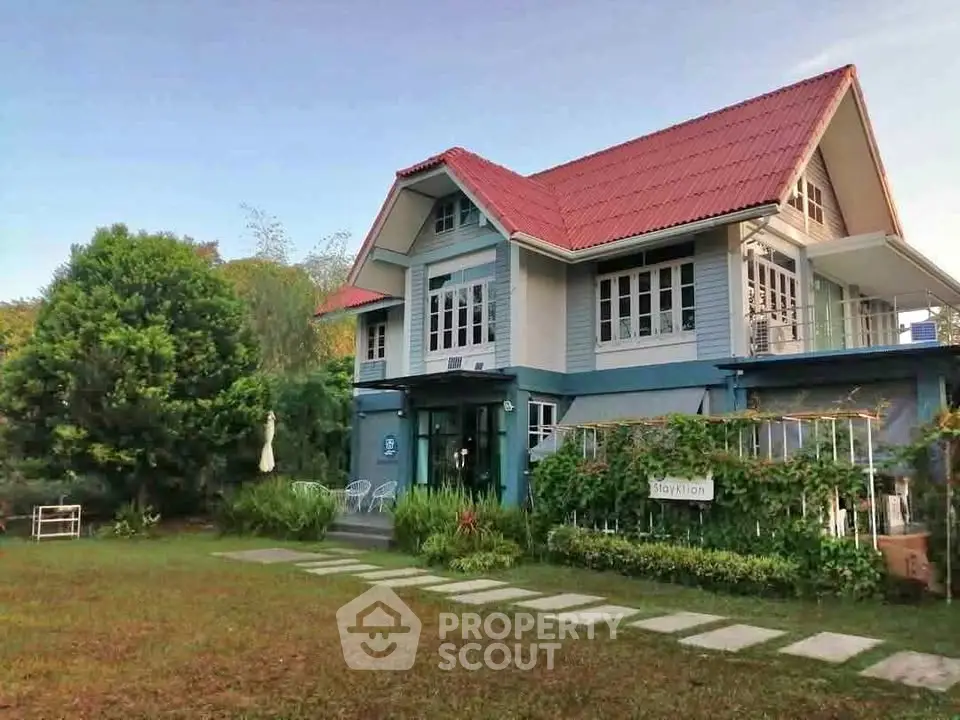 Charming two-story house with red roof and lush garden, perfect for serene living.