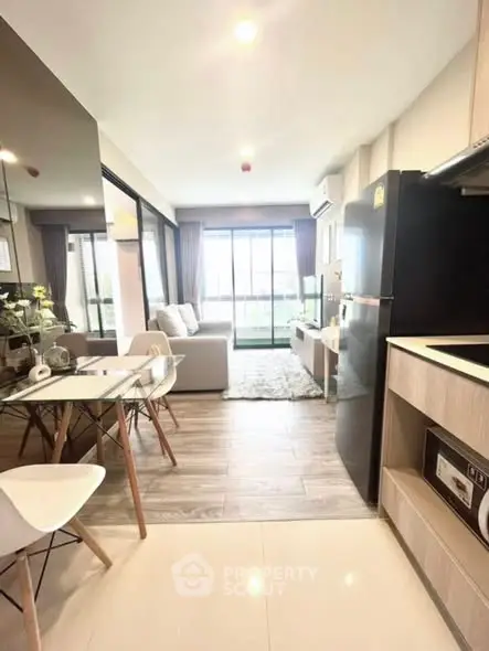 Modern open-plan living room with kitchen and balcony view, featuring sleek furniture and natural light.
