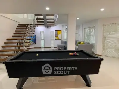 Modern living room with pool table and stylish staircase in open-plan home.