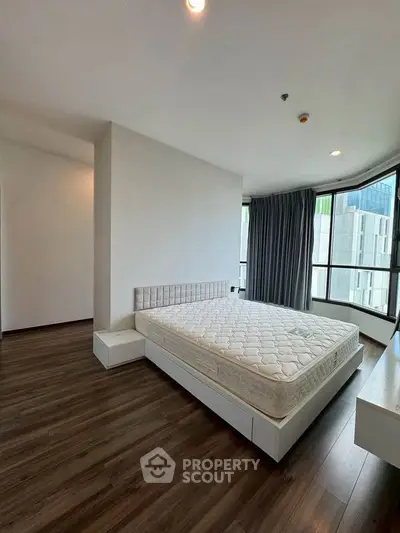 Spacious modern bedroom with large windows and hardwood floors in a high-rise apartment.