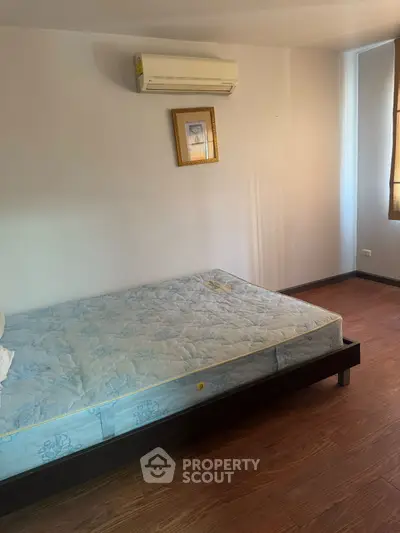 Cozy bedroom with wooden flooring and wall-mounted air conditioner, perfect for a comfortable living space.