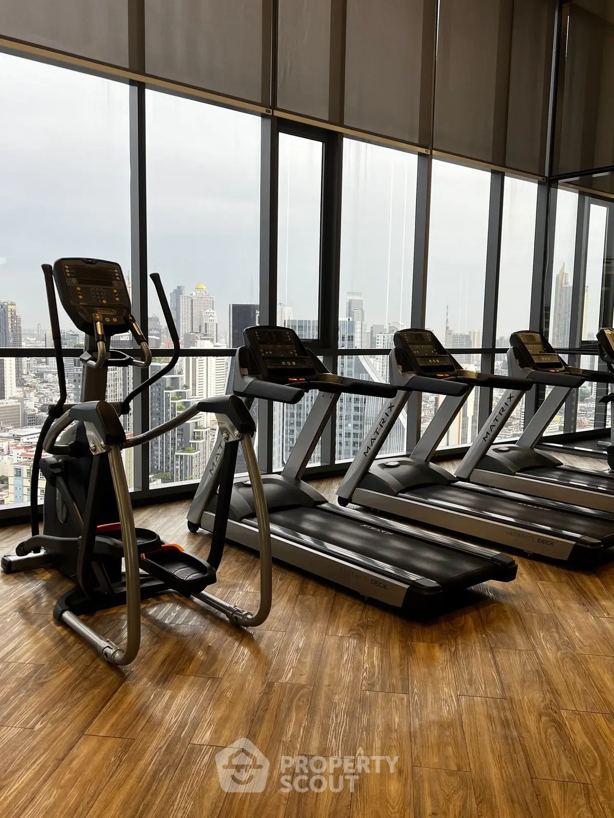 Modern gym with city view featuring treadmills and elliptical on wooden floor.
