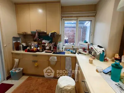 Cozy kitchen with cluttered countertops and window view, featuring beige cabinets and modern appliances.