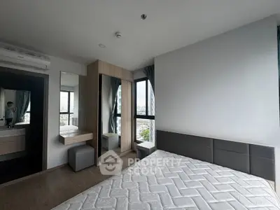 Modern bedroom with large windows and city view, featuring a stylish wardrobe and vanity area.