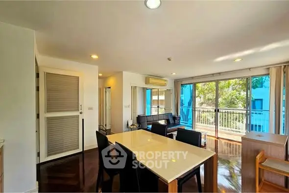Spacious living room with large windows and balcony access, featuring modern furniture and natural light.