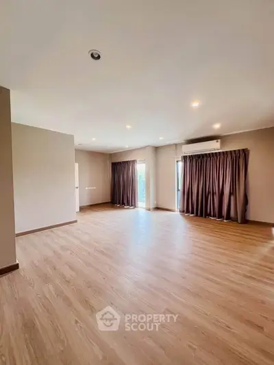 Spacious empty living room with wooden flooring and large windows for natural light.