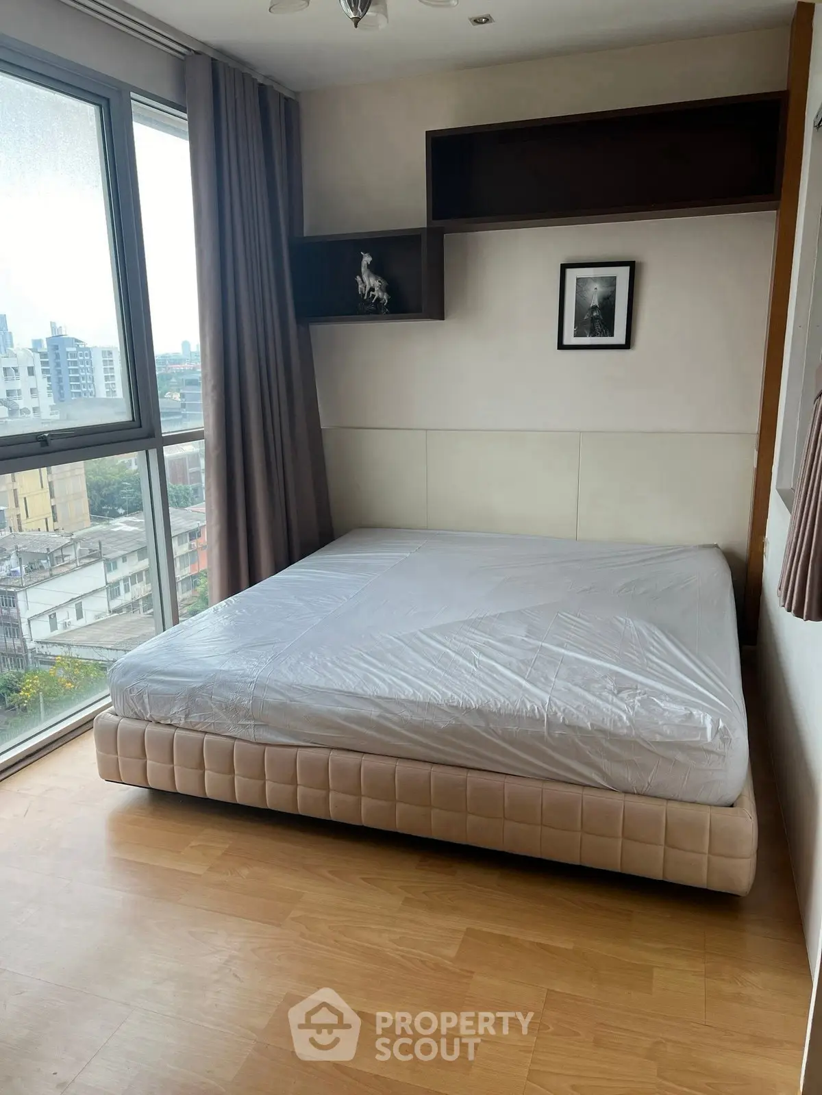 Spacious bedroom with large window offering city views, featuring a comfortable bed and elegant decor.