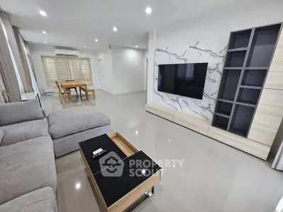 Spacious modern living room with sleek furniture and large TV, perfect for relaxation and entertainment.
