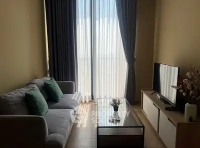 Cozy living room with modern sofa, TV, and floor-to-ceiling windows offering natural light.