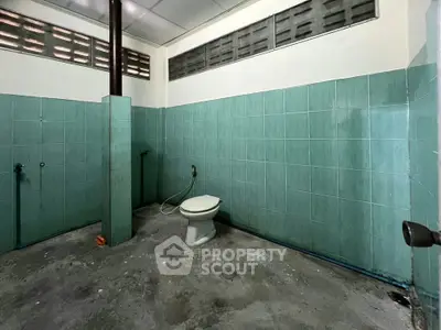 Spacious bathroom with teal tiles and basic fixtures, ideal for renovation opportunities.