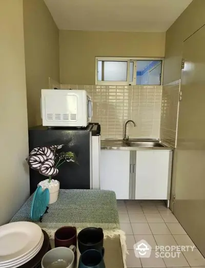 Compact kitchen with microwave, sink, and tiled backsplash in cozy apartment.