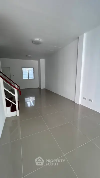 Spacious empty room with glossy tiled flooring and staircase, ideal for customization.