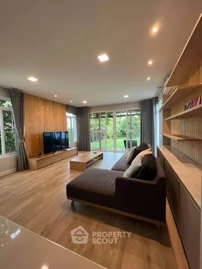 Spacious modern living room with large windows and garden view, featuring sleek wooden floors and contemporary furniture.