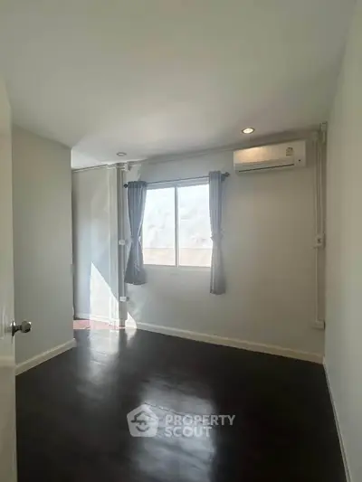 Spacious bedroom with dark wood flooring and natural light from large window.