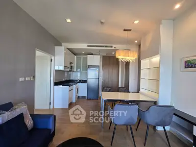 Modern open-plan living room with sleek kitchen and dining area, featuring elegant lighting and contemporary furniture.