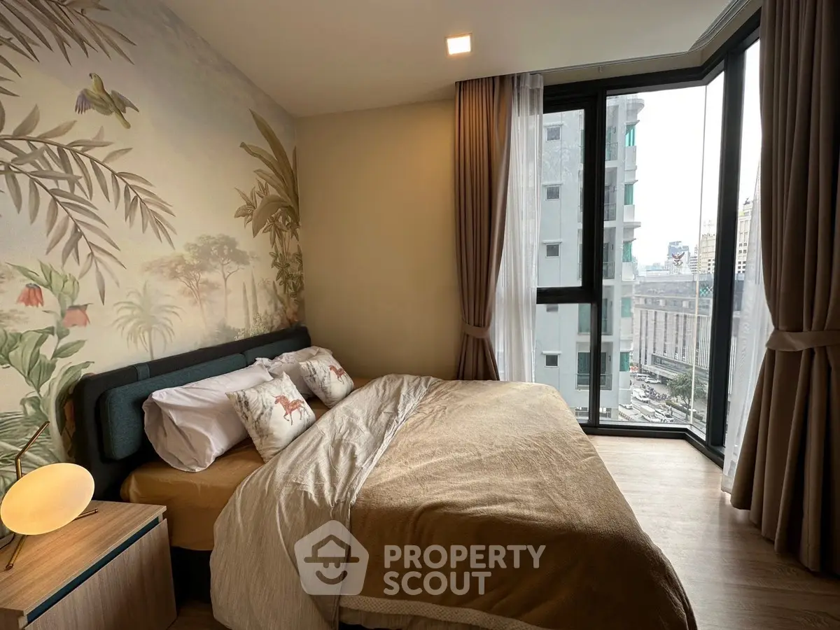 Cozy bedroom with large windows and city view, featuring stylish decor and comfortable bedding.