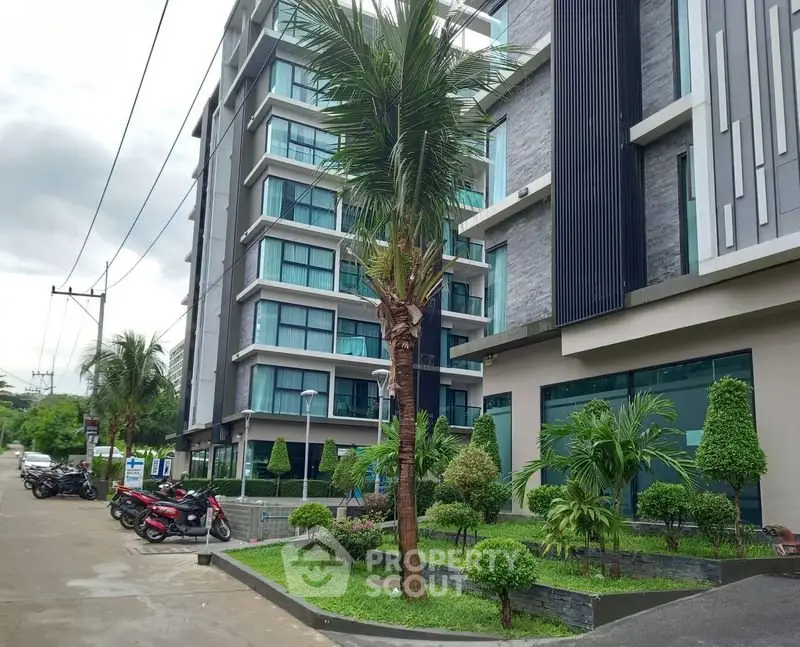 Modern apartment building exterior with lush landscaping and palm trees.