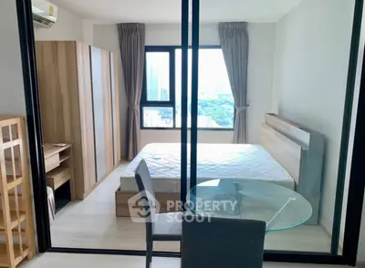 Modern bedroom with city view, featuring glass partition and stylish furnishings.