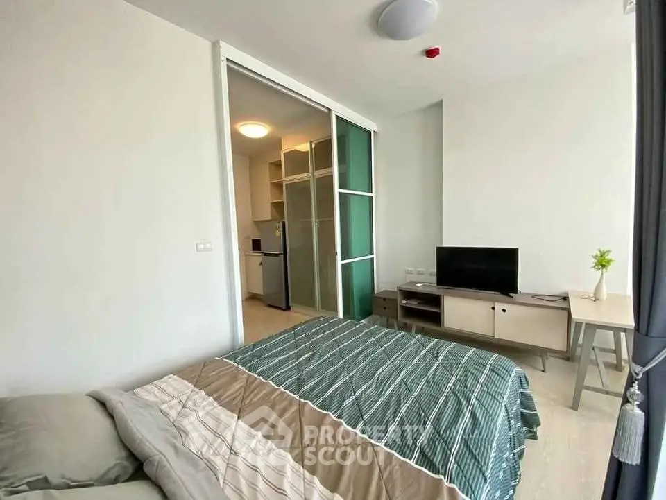 Modern bedroom with sliding glass doors leading to a compact kitchen area, featuring a cozy bed and a TV stand.