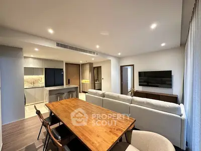 Modern open-plan living room with sleek kitchen and dining area, featuring stylish furniture and ambient lighting.