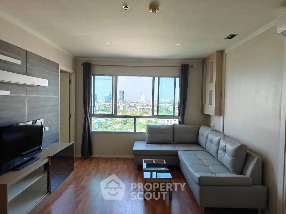 Modern living room with large window and city view, featuring sleek furniture and wooden flooring.