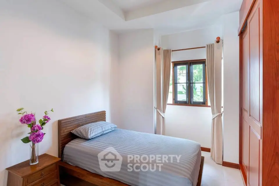 Cozy bedroom with single bed and wooden wardrobe, bright window view.