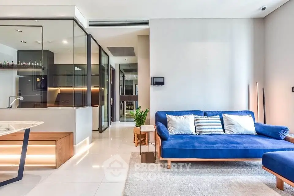 Modern living room with blue sofa and open kitchen layout, featuring sleek glass partitions and stylish decor.