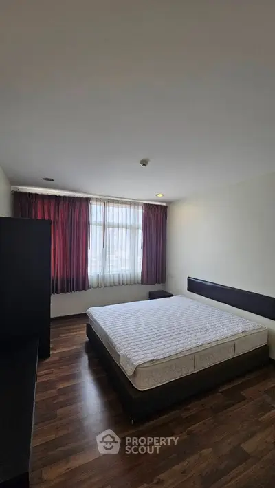 Spacious bedroom with large window and wooden flooring in modern apartment