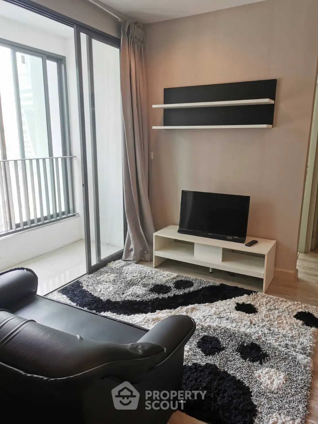 Modern living room with sleek black armchair, TV, and stylish rug in a bright apartment.