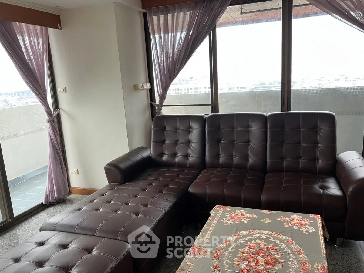 Spacious living room with leather sofa and large windows offering city views
