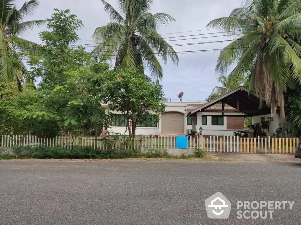 Charming single-story home nestled among lush palm trees, featuring a spacious yard and cozy covered porch, ideal for tranquil living.