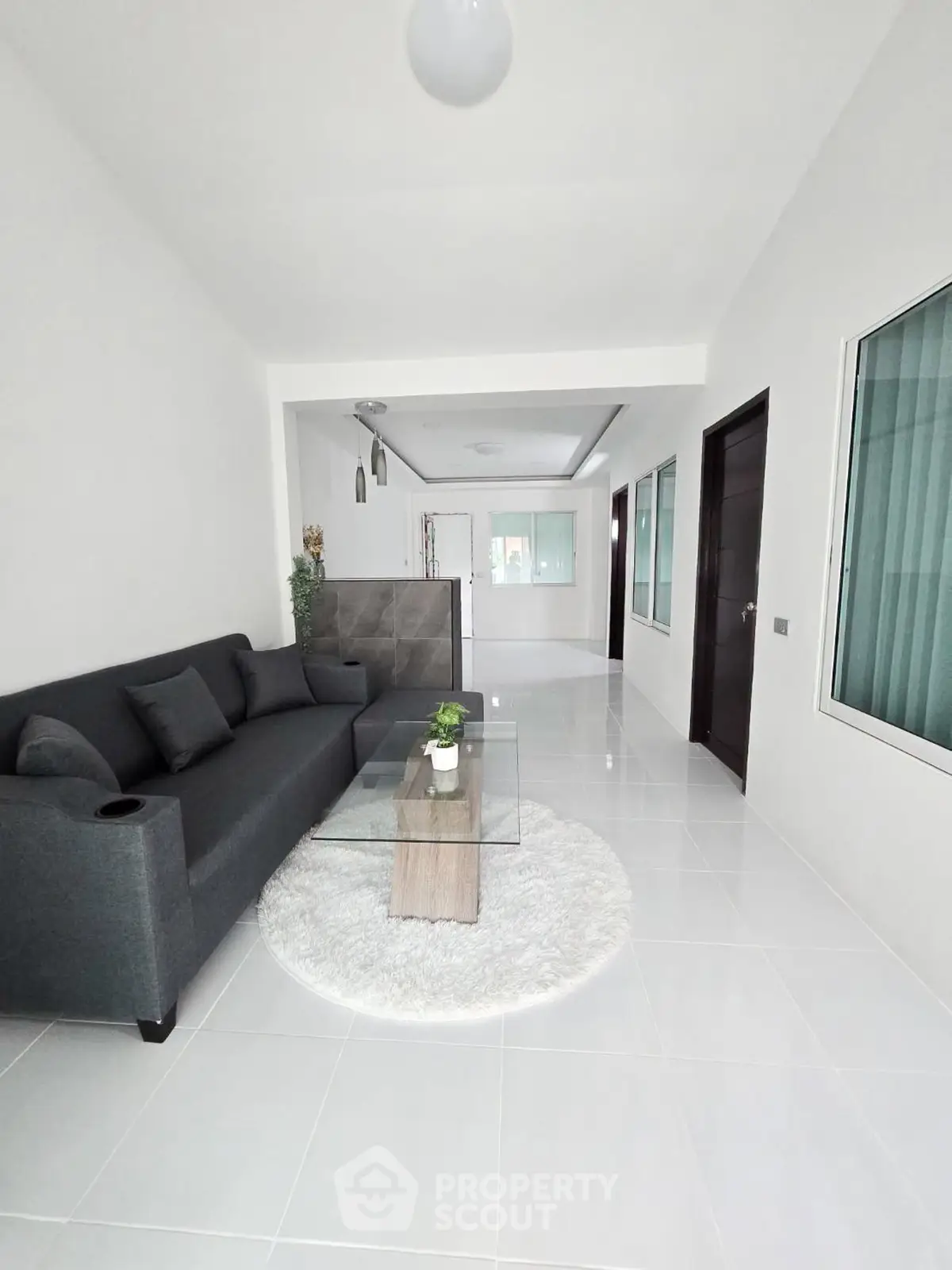 Modern living room with sleek gray sofa and glass coffee table on white rug, bright and spacious.