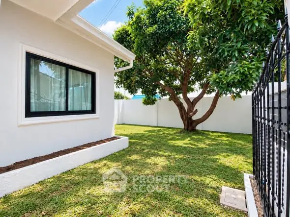 Charming backyard with lush green lawn and mature tree beside a modern house.
