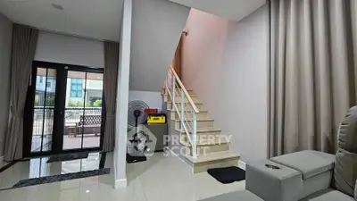 Modern living room with staircase and balcony view, featuring sleek furniture and elegant curtains.