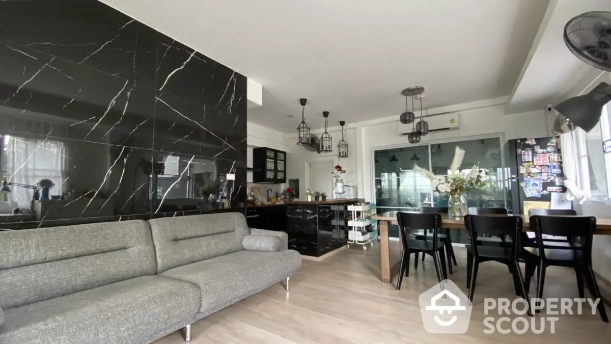 Modern open-concept living and dining area with sleek black marble accent wall and stylish furniture.