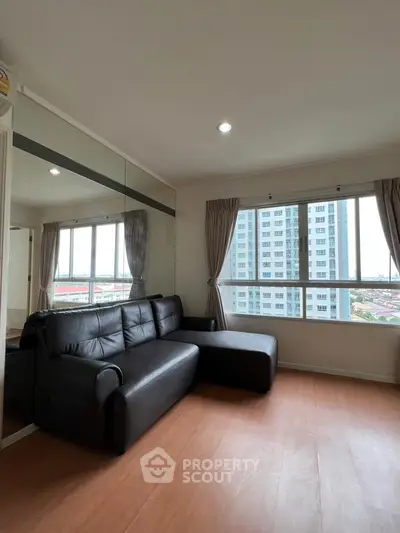 Modern living room with black leather sofa and large windows offering city views.
