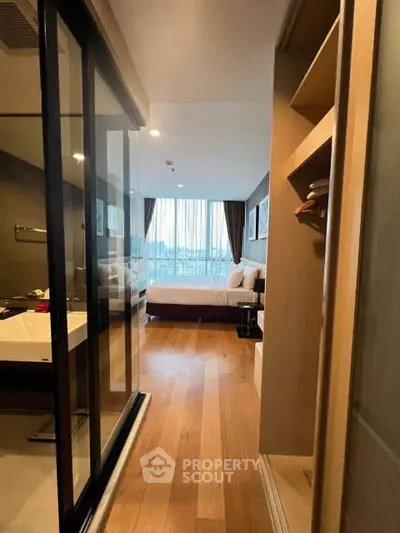 Modern bedroom with ensuite bathroom and wooden flooring, featuring large windows and stylish decor.