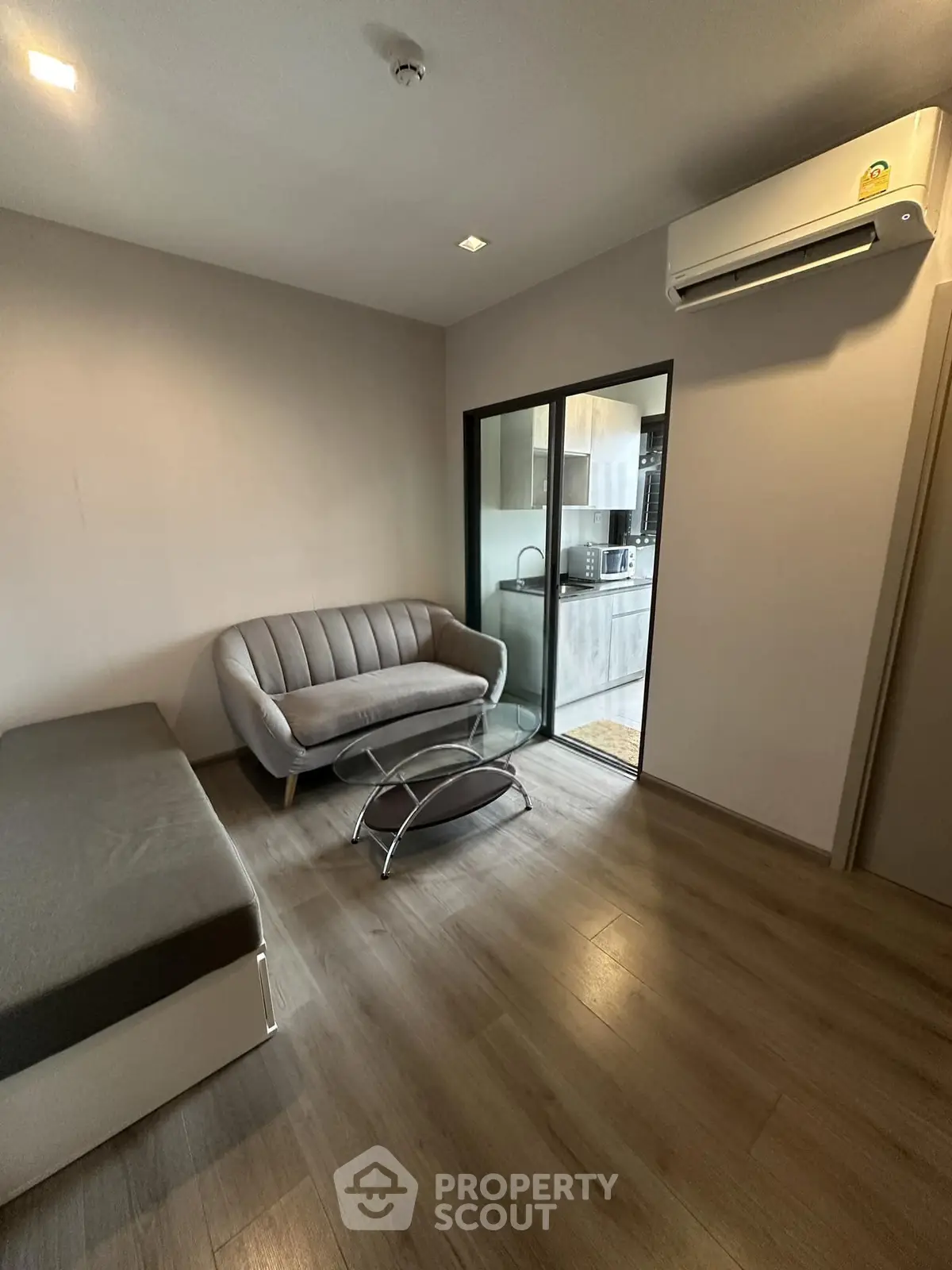 Modern living room with sleek sofa and glass partition leading to kitchen