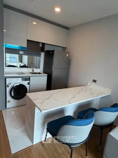Modern kitchen with sleek marble island and built-in washing machine in compact apartment.