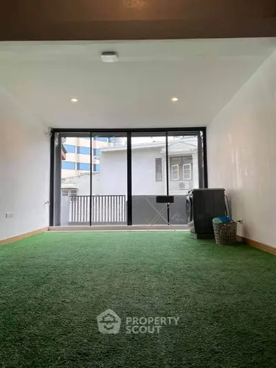 Spacious room with artificial grass flooring and large windows offering urban views.