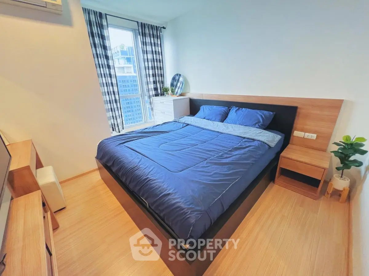 Modern bedroom with blue bedding and city view, featuring wooden furniture and stylish decor.