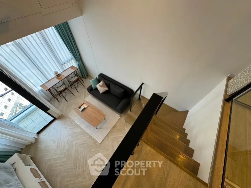 Modern loft apartment with stylish living room and staircase, featuring large windows and elegant decor.