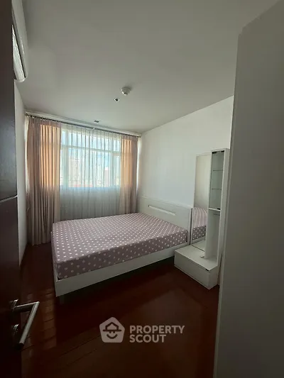 Cozy bedroom with natural light and elegant curtains, featuring a comfortable bed and sleek wooden flooring.