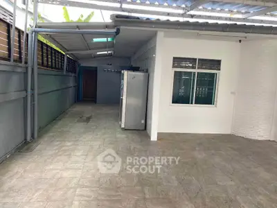 Spacious covered outdoor area with tiled flooring and refrigerator, ideal for versatile use.