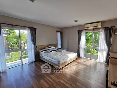 Spacious bedroom with large windows and garden view, featuring wooden flooring and modern decor.
