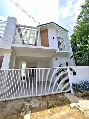 Modern white two-story house with gated entrance and lush greenery