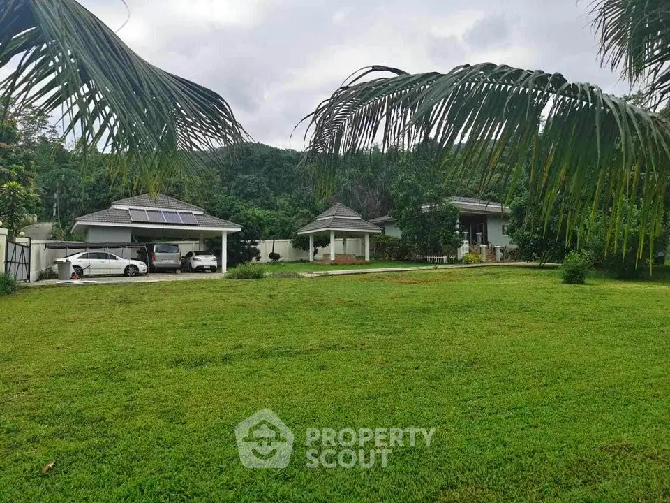 Lush tropical oasis with spacious lawn and twin single-story homes featuring covered parking and serene mountain backdrop.