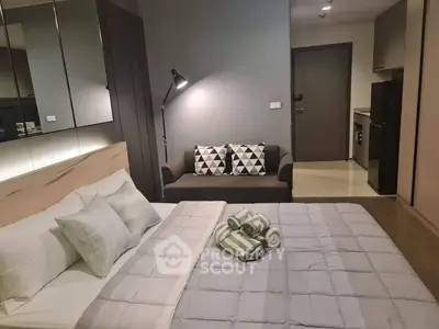 Modern bedroom with cozy bed, stylish sofa, and sleek kitchen area in open layout apartment.