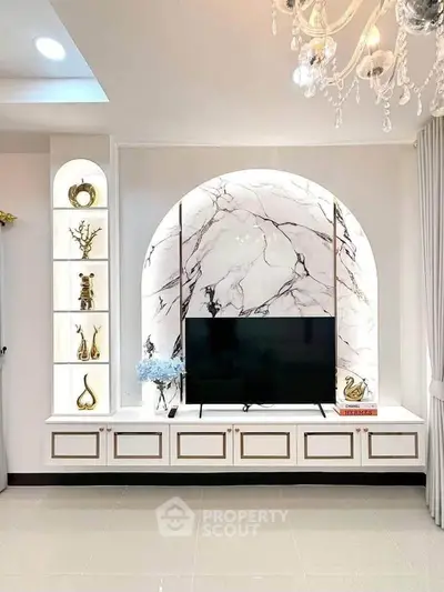 Luxurious living room with elegant TV unit and marble backdrop, featuring stylish decor and chandelier lighting.